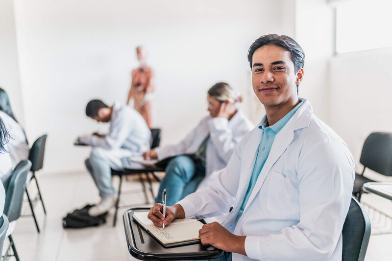 Male PA student in white jacket looking confidently at camera in a live classroom setting
