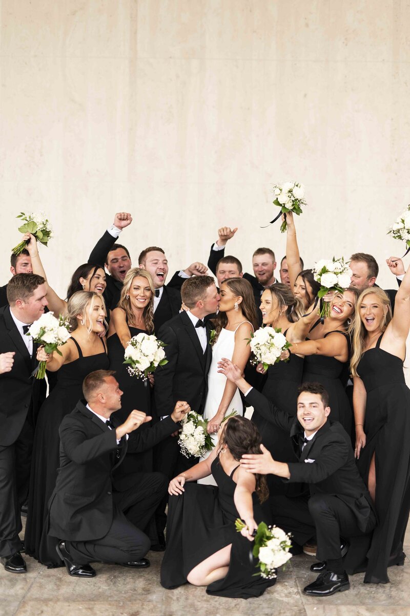 Bride and groom kissing in front of the wedding party