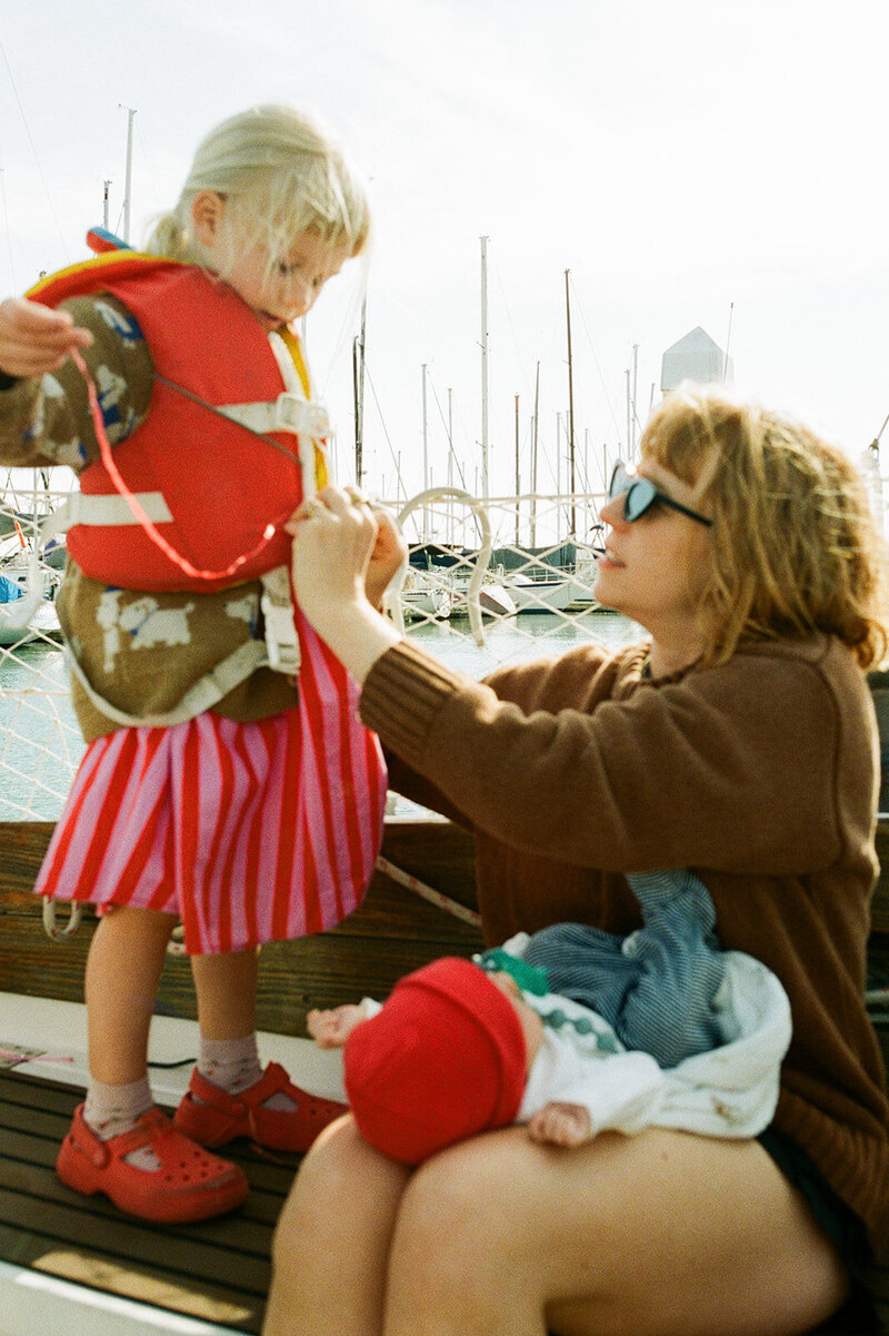 out of focus photo of mom with newborn in her lap helping daughter with lifejacket