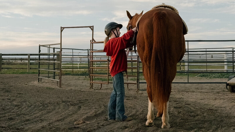 A child gently holding a horse she’s about to ride at Spirit's Respite Ranch, surrounded by the peaceful rolling hills near Stettler, Alberta.