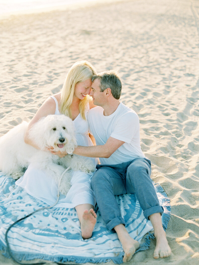 A couple snuggling with their fluffy white dog on the beach in Ventura County