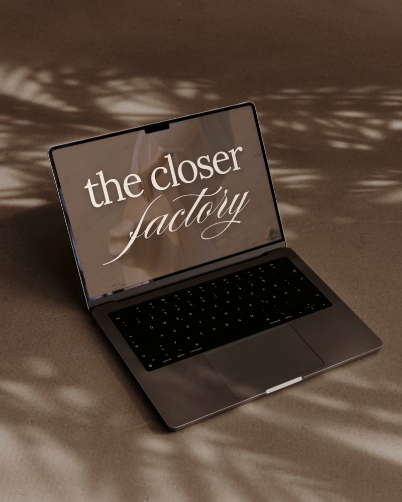 Laptop on a warm-toned surface displaying 'The Closer Factory' text, surrounded by soft shadows