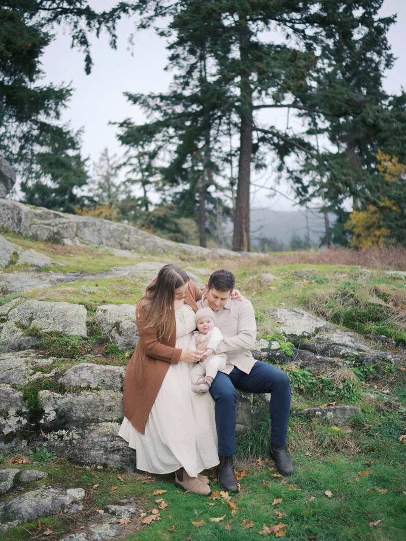 Mother, father and baby seated on a rock in Caulfield Park during their family session 