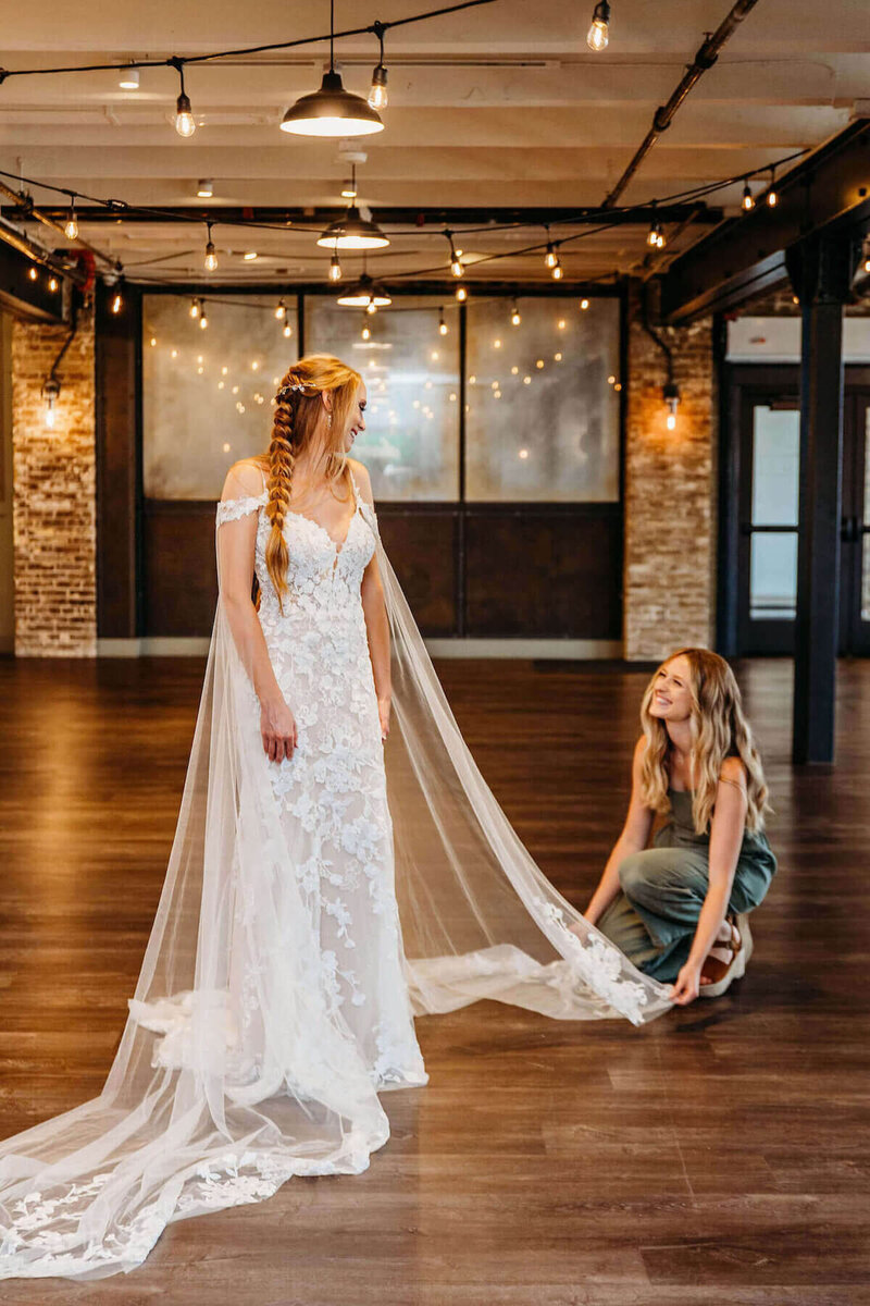 Liz, owner of Dream Weddings, wedding planner wisconsin, smiling up at a bride fixing her veil at The Gage in West Allis.