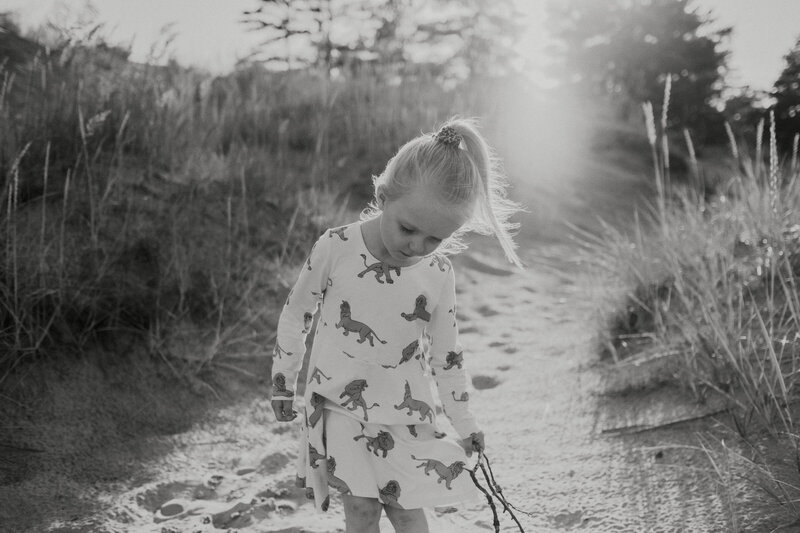Family photograph of a 4-year old girl who is looking down with a stick in her hand at the sand dunes in Yyteri in Finland