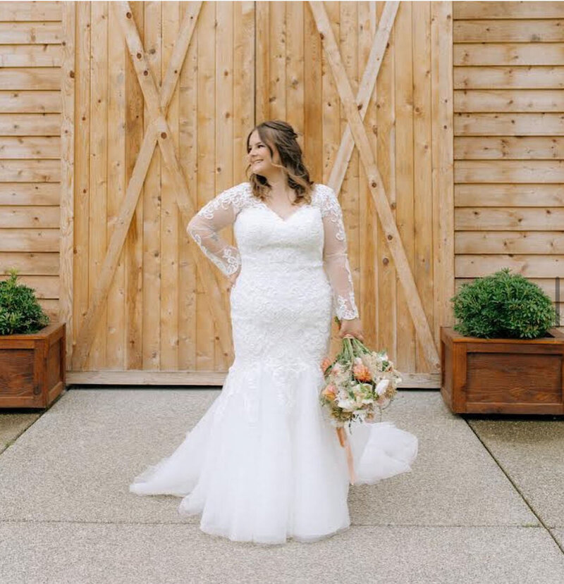 A bride posing confidently in a fitted lace gown in front of wooden doors