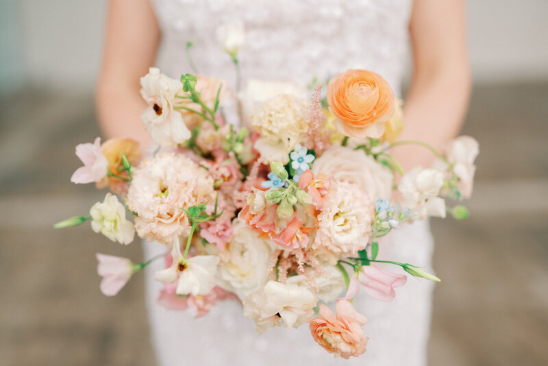 Bride holds her colorful wedding bouquet that is decked out in spring florals taken by Lacey Graham a luxury wedding photographer in Illinois