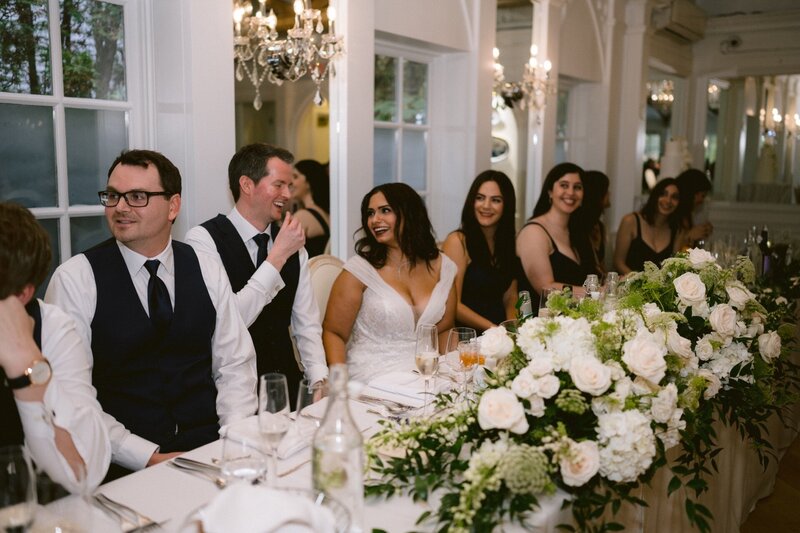 Guests seated at a wedding reception table adorned with white floral arrangements.