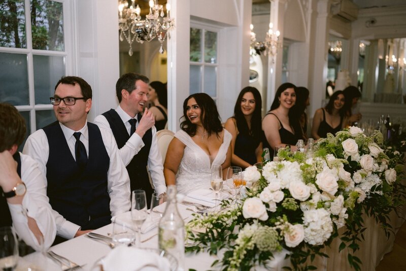 Guests seated at a wedding reception table adorned with white floral arrangements.