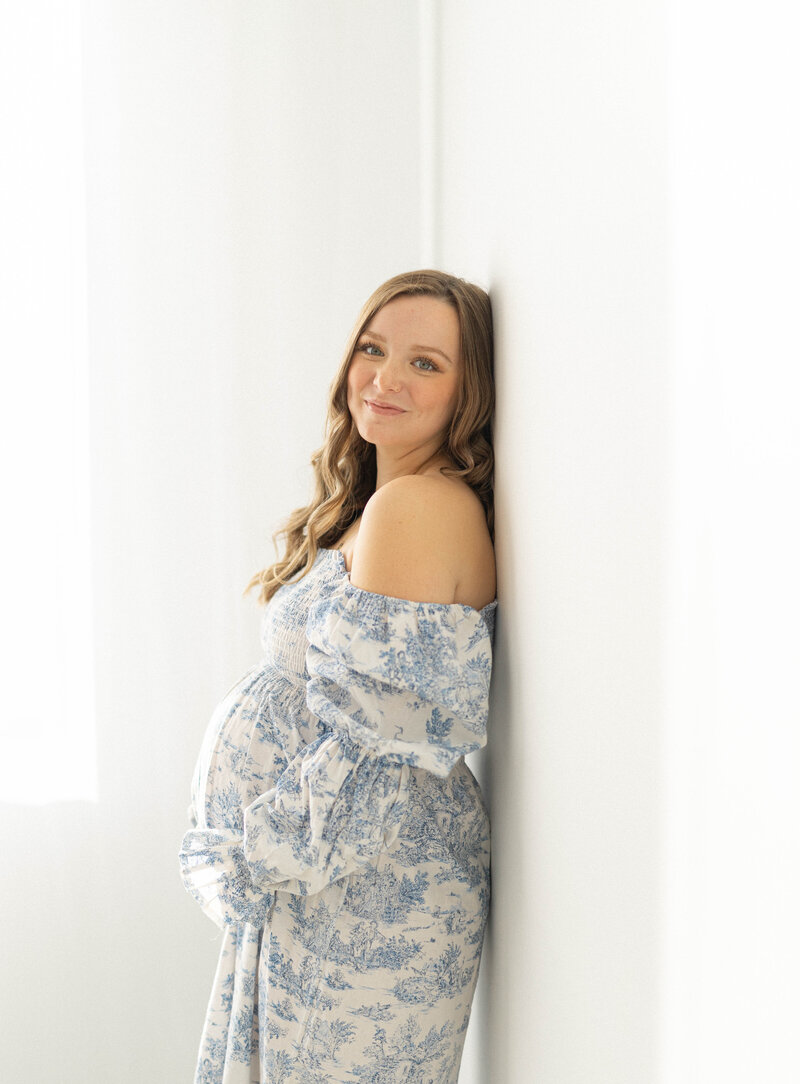 bright studio image of pregnant  women holding belly and leaning against the wall