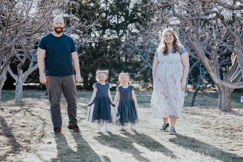 Idaho Falls maternity photos with mother and father holding hands with their two daughters in an orchard during the fall