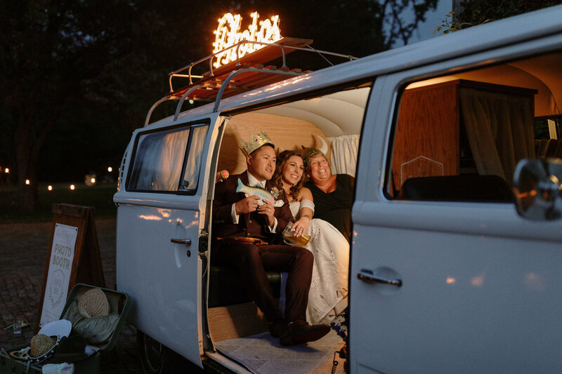 A vintage white van serves as a whimsical photo booth at twilight, with playful decorations and props scattered nearby.