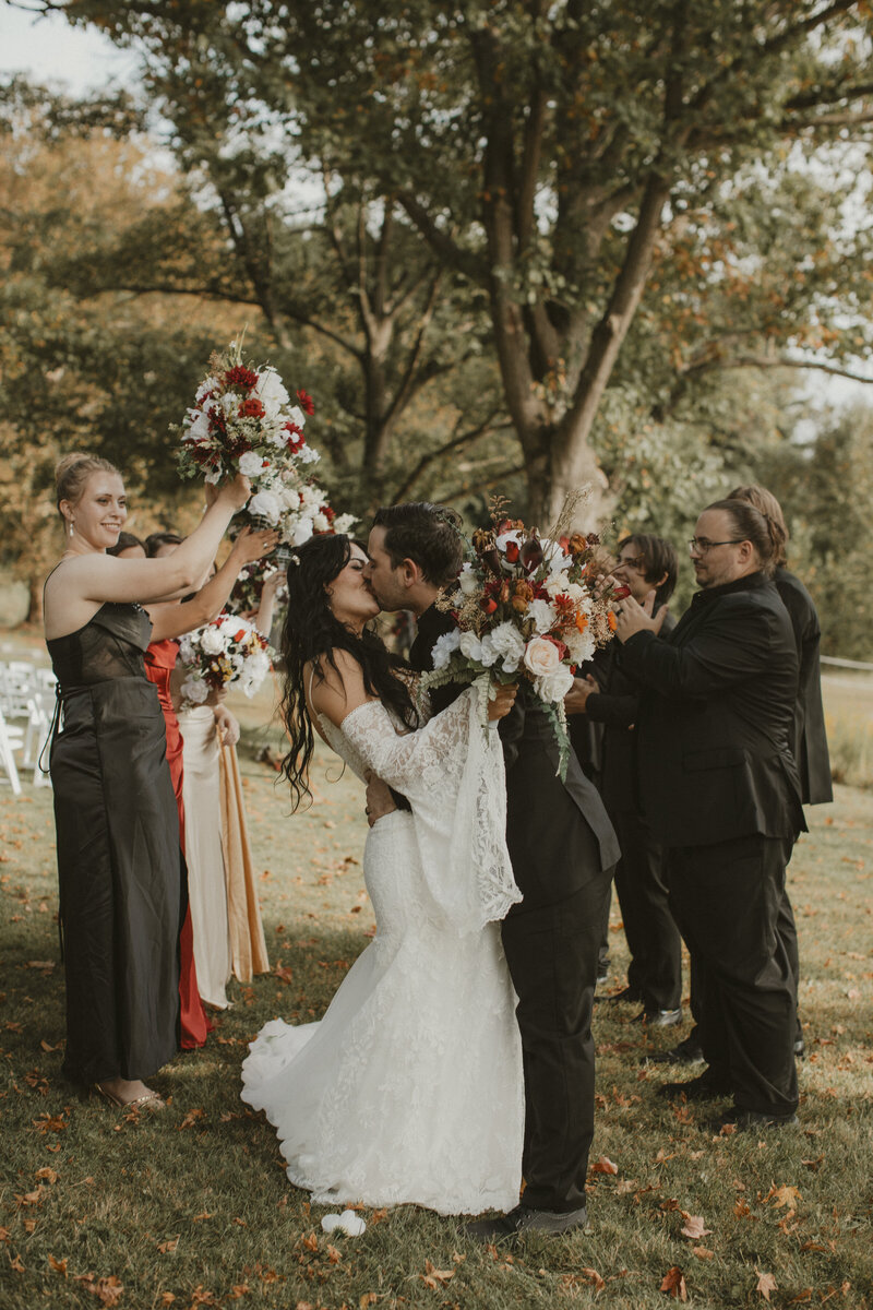 Bride and groom celebrating with friends outside among autumn leaves during a joyful wedding portrait session