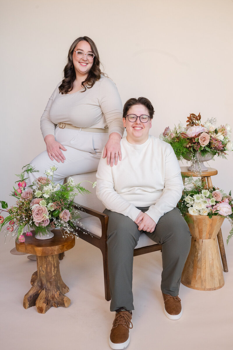 Three people sitting and standing together with flowers on stools around them