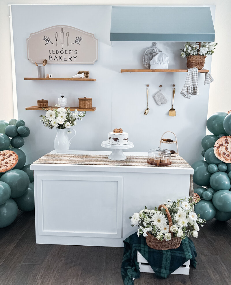 Bakery wall with decorated shelves, blue balloons, white flowers and baking tools.