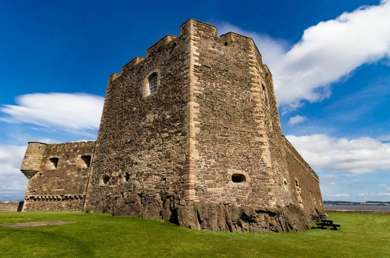 Stone walls of Dalhousie Castle rising against a bright blue sky near Edinburgh — the final stay on Kat Mackenzie’s Work in Progress Literary Tour, where travelers dine like royalty and close their story with a touch of Scottish magic.