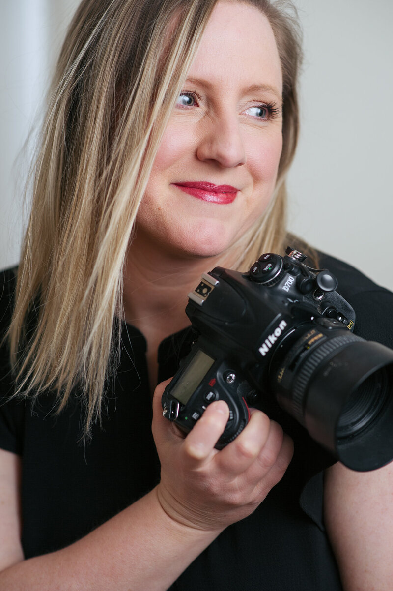 Headshot of Boston branding photographer Kristin Palkoner holding her Nikon D700 with 50 mm lens.