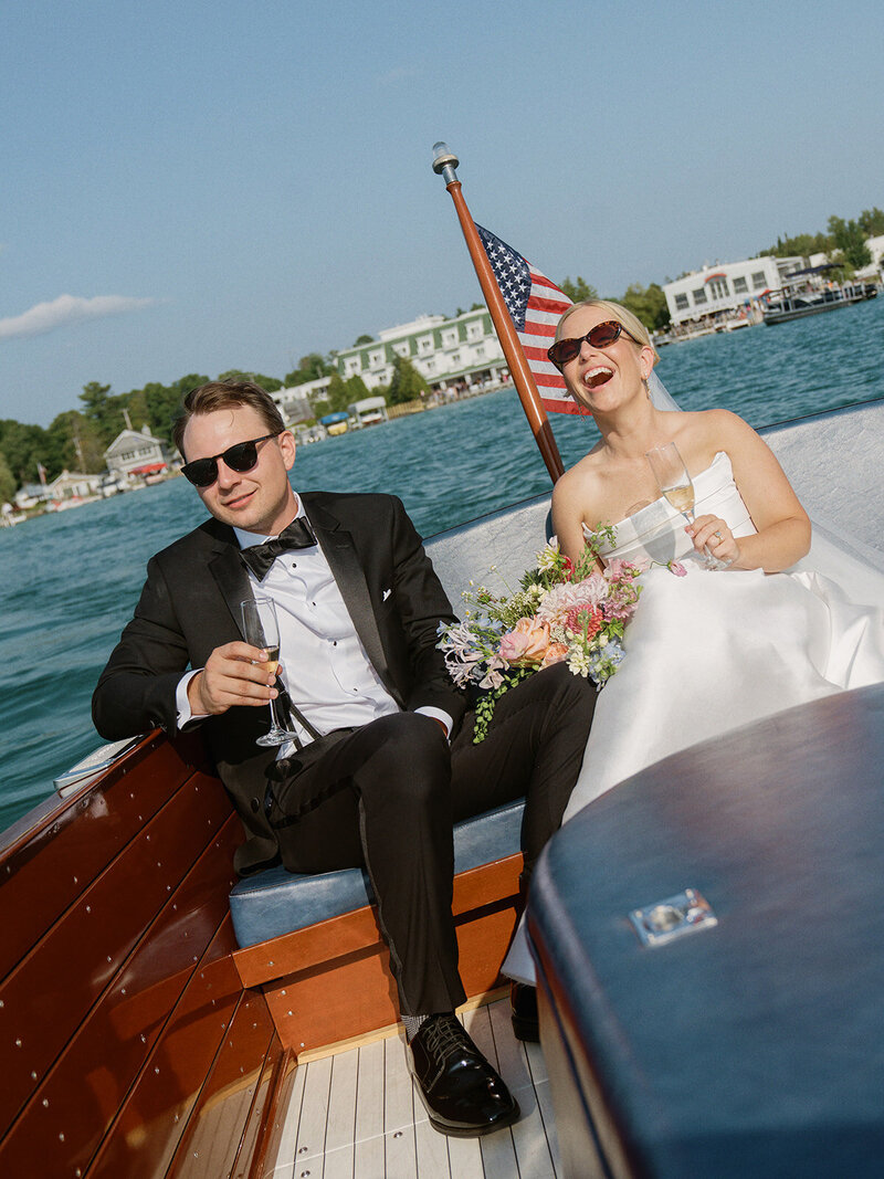 A joyful bride laughs towards the camera with her husband behind her.