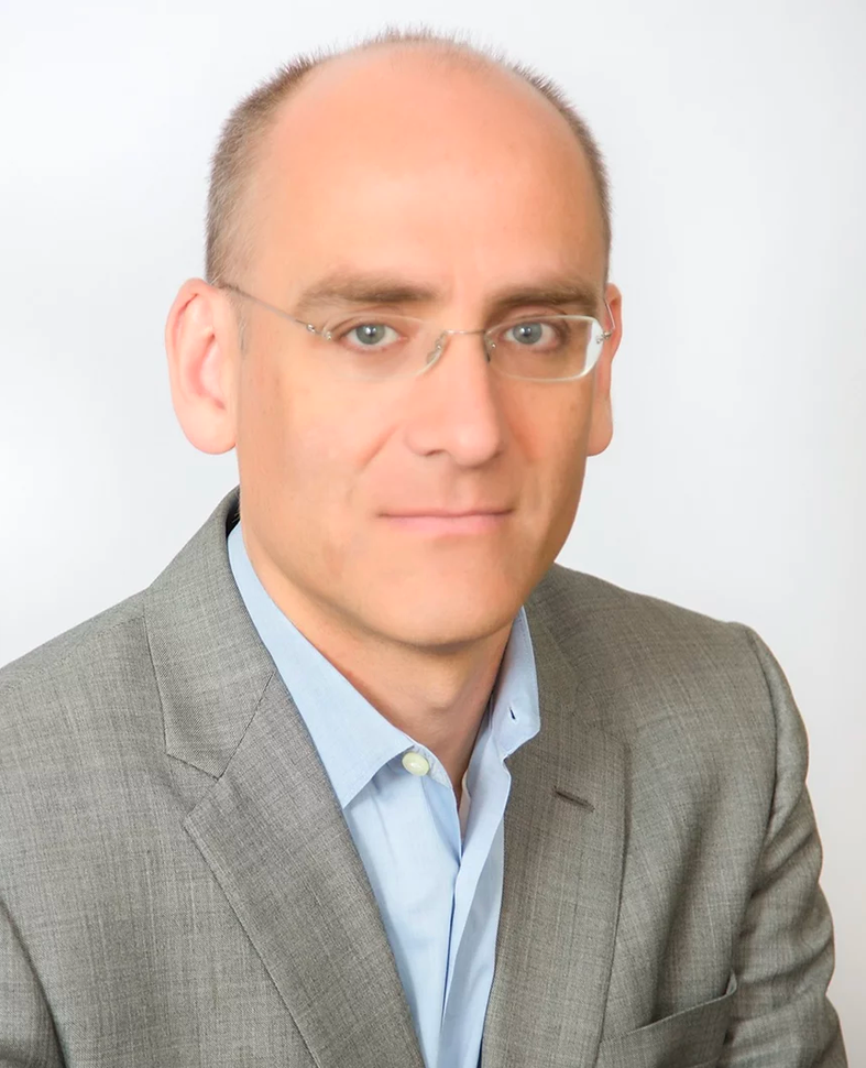 Headshot of Steve, a Film & Ink Attorney. He has a closely shaven head, light eyes with rimless glasses, and is wearing a gray suit jacket and light blue shirt.