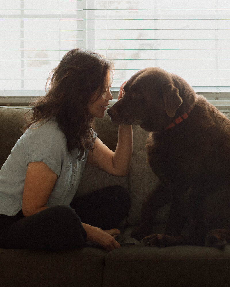 Outdoor portrait of a woman and her chocolate Labrador, both looking at the camera, taken in Menifee, California.