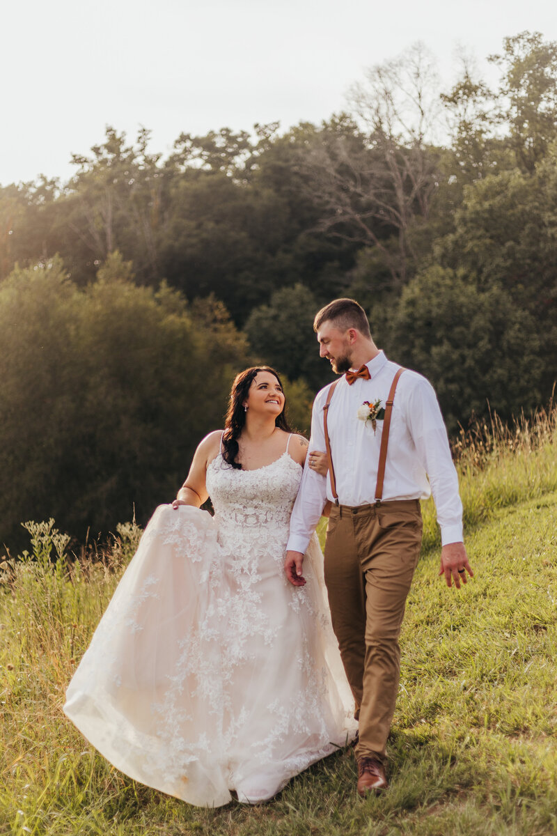 bride looks at groom adoringly while walking through an East Tennessee field in summertime