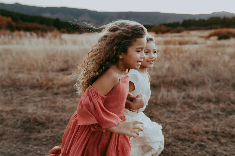 Two gorgeous sisters run through a field in Denver Colorado while wearing beautiful BoHo dresses. One is wearing a cream color dress while the other is in Coral. Both perfectly match the fall mountain backdrop.