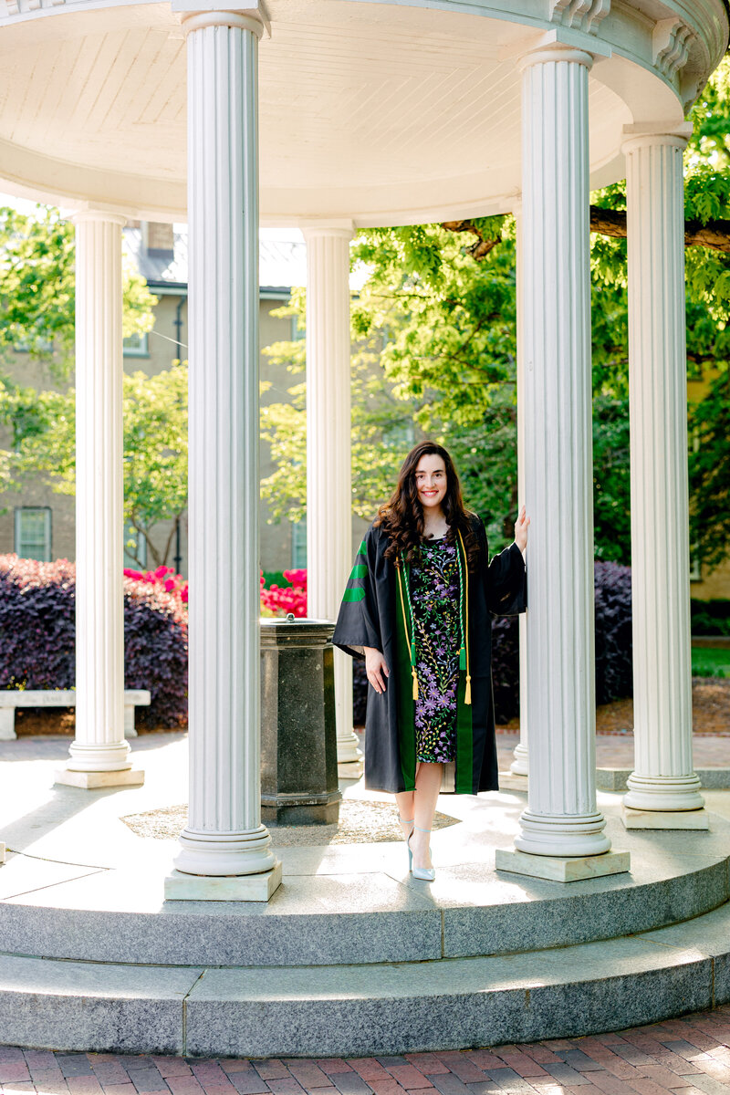 Graduate in academic regalia celebrating at a university landmark during a portrait session.