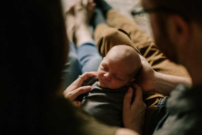parents looking down at their newborn in their lap at home 