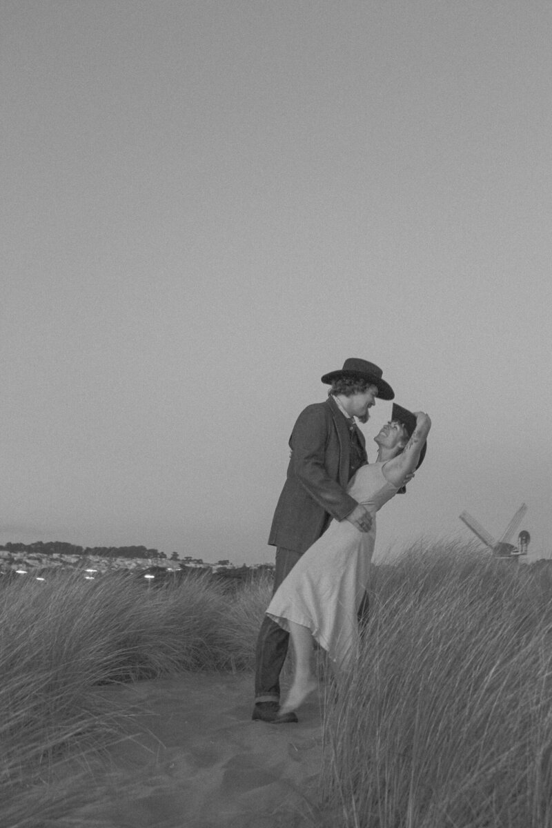 cowboy aesthetic playful engagement photos in san francisco california with couple kissing in the dunes