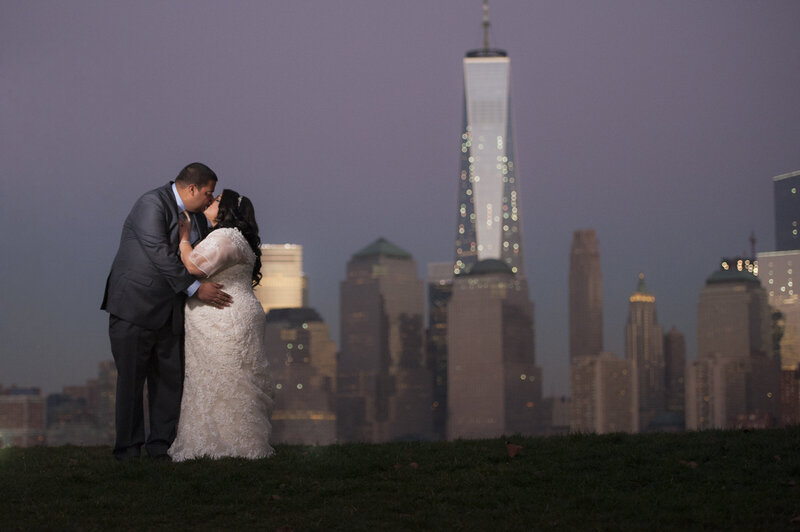 A newlywed couple kissing with a city skyline behind them 