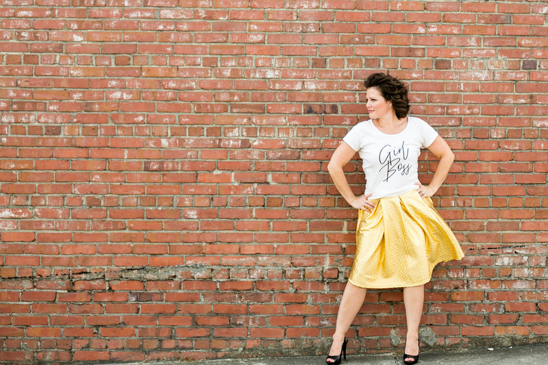 Empowered brunette female business owner strikes a pose during brand photography session in front of brick wall