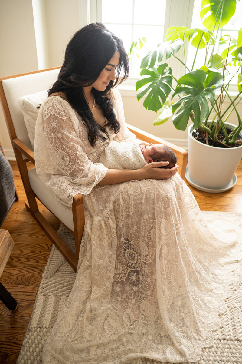 Mom in white lace dress, holding her newborn son in her home in Ottawa
