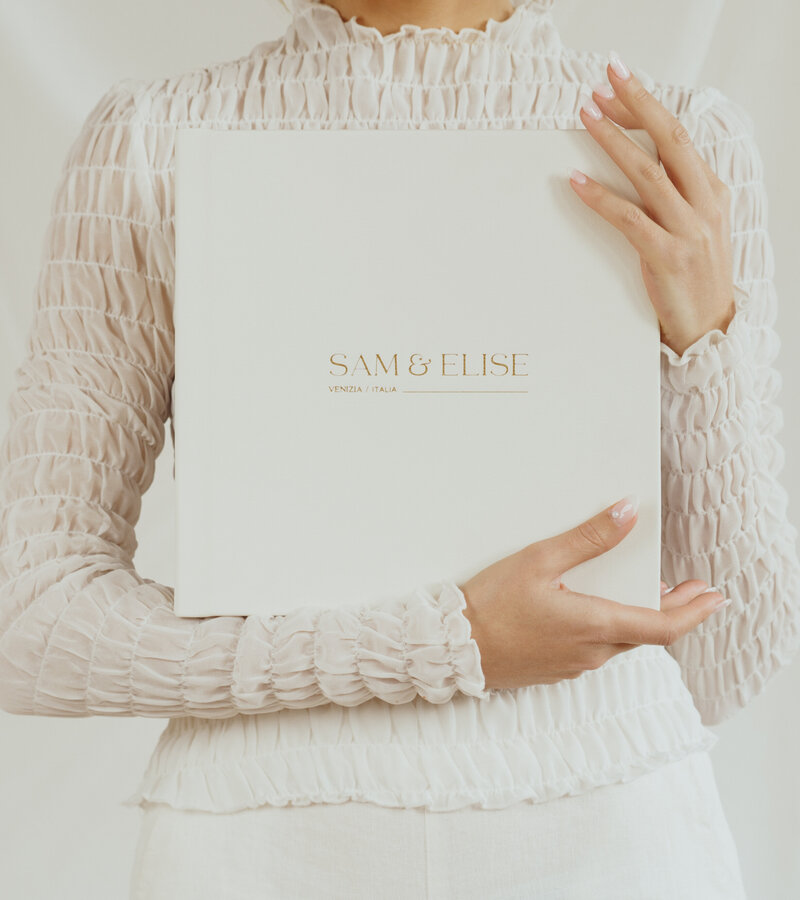 Woman dressed in white holding large white eco leather heirloom wedding book to chest- Romero Album Design