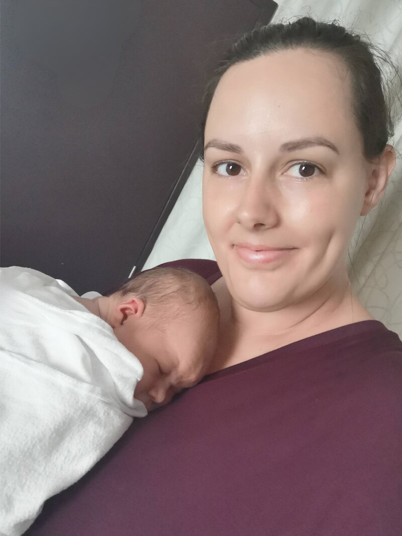 Claire is smiling and holding a newborn baby, wrapped in a white blanket.