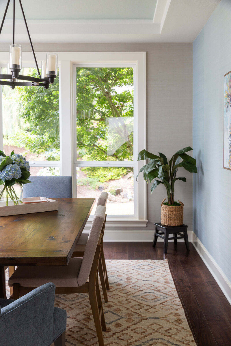 A dining room showcasing a modern farmhouse interior design, featuring a wooden dining room table, hanging light fixture and windows.
