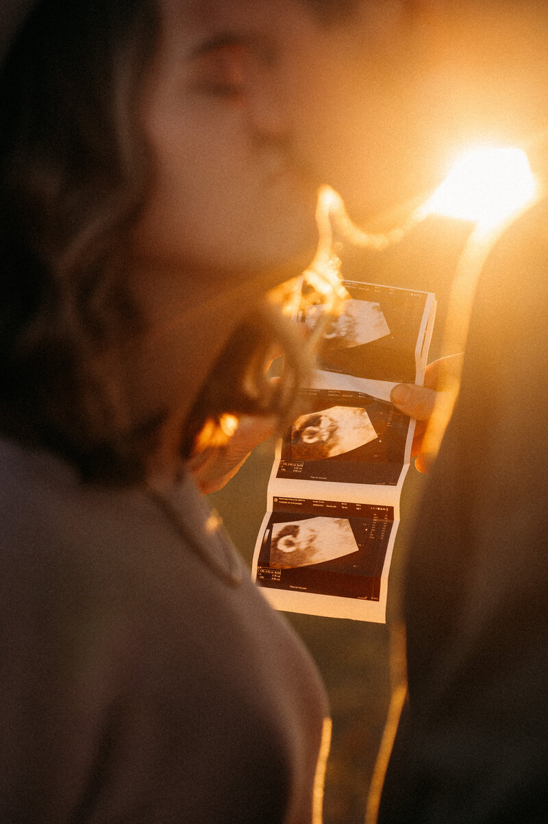 An expecting couple share a kiss while holding their sonogram photo. 