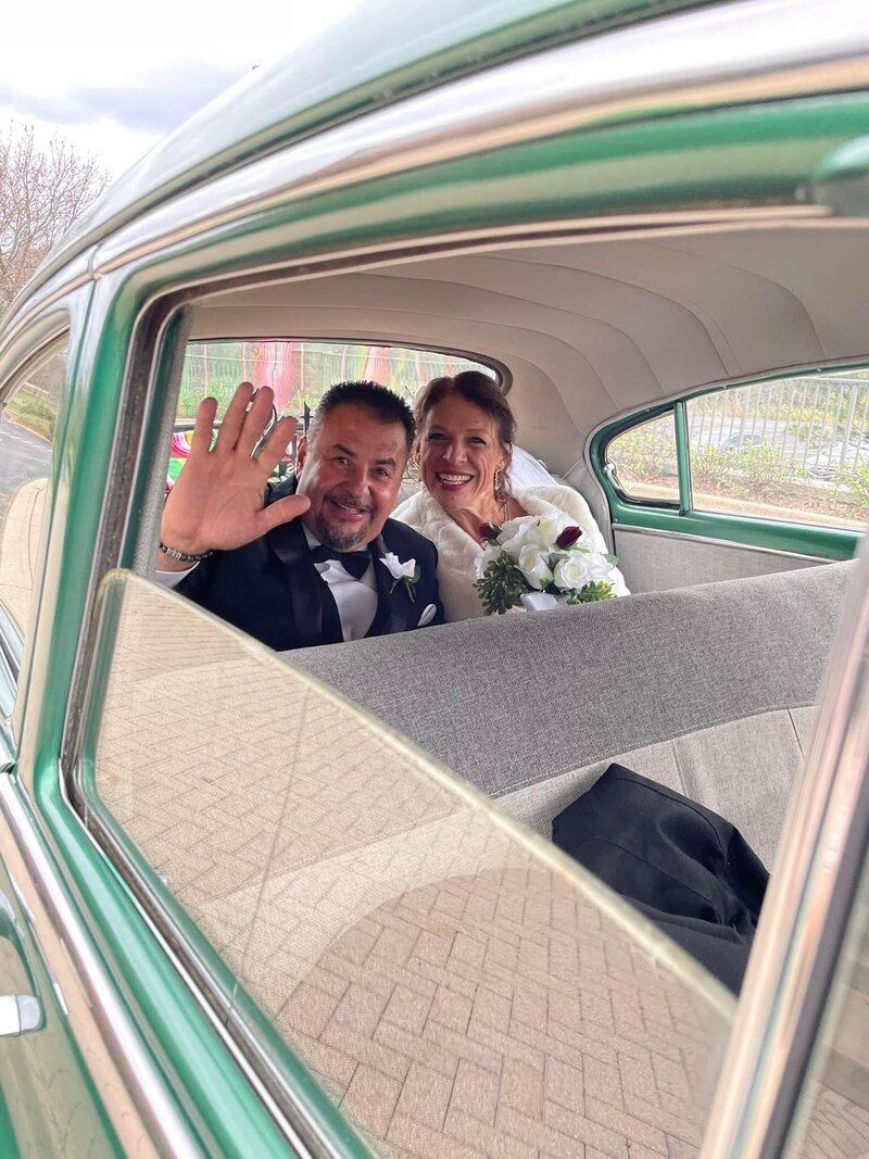 bride and groom in vintage car waiving to guests for send-off