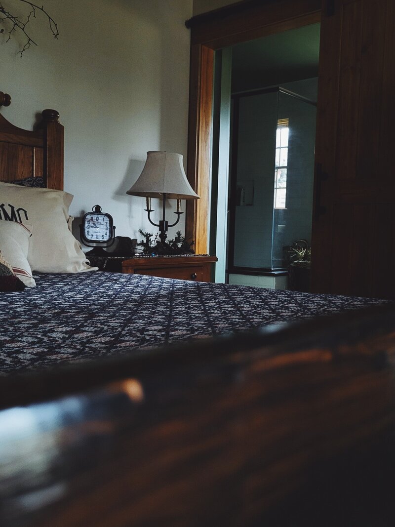 view of an oak bed, nightstand candlelamp into the newly renovated bathroom shower
