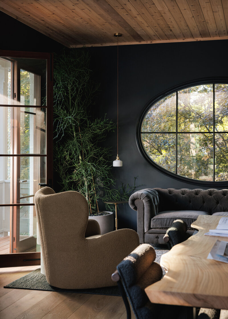 Moody navy blue office with oval window, strong architecture, warm wood ceiling with draping soft light