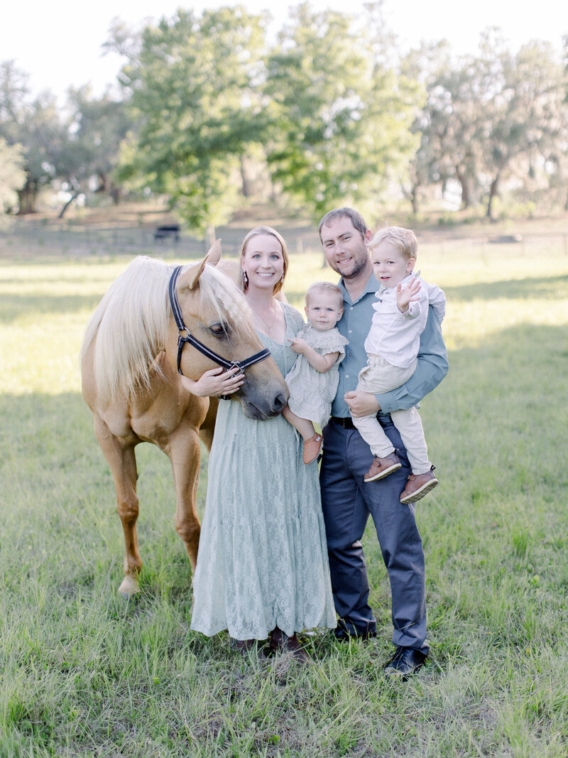 Family portrait of mom, dad, 4 year old boy, 1 year old girl and palomino horse on a horse farm in soft afternoon golden light by NH family photographer Fieldstone Studio.
