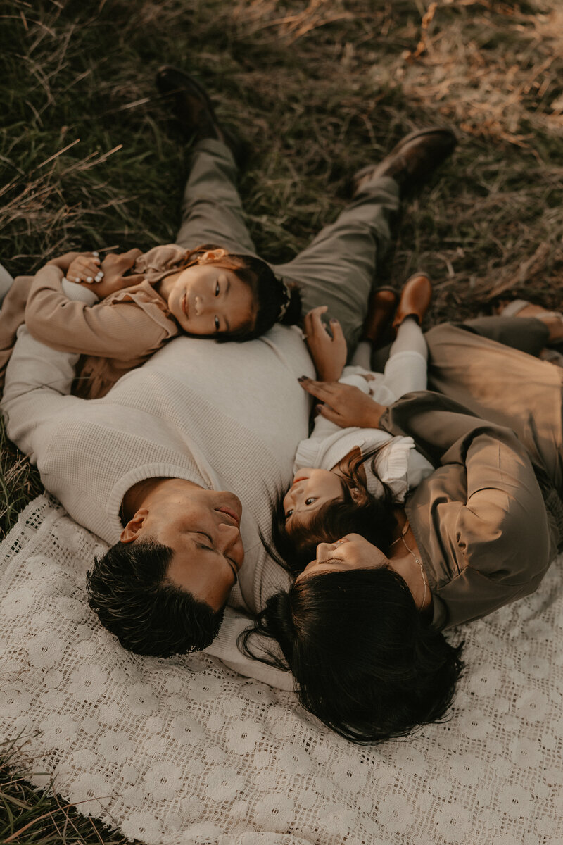 Family enjoying a playful outdoor sunset session in Peapack, NJ, with parents and children interacting joyfully in a grassy field, captured by Burkat Photography.