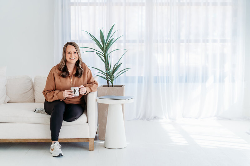 Kim sitting on the couch smiling as she holds a cup of coffee