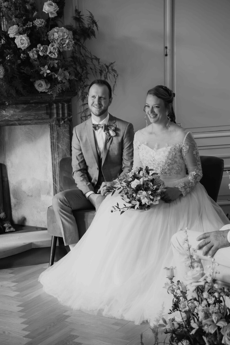 Bruid en bruidegom tijdens hun ceremonie in zwart-wit, met bruidsboeket bij de openhaard, perfect gepland door een weddingplanner.