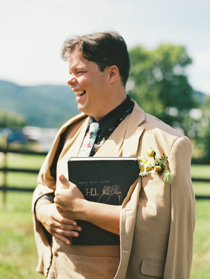 A candid moment with the officiant holding the ceremony book who sees the groom and puppy for the first time in their wedding attire, by film photographer Megan Lynn of My Sun and Stars Co.