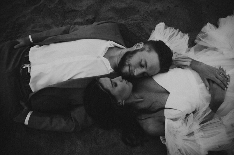 Black and white photo of bride and groom laying down on beach