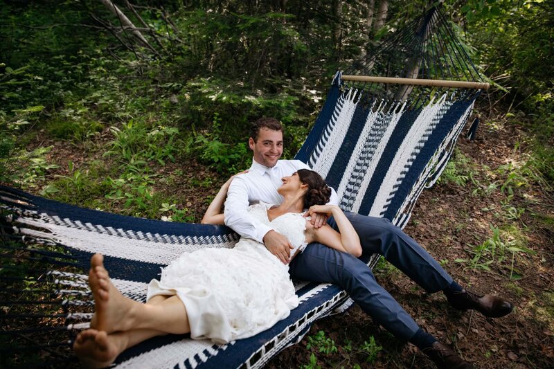 A wedding couple smiling while laying on a hammock together.