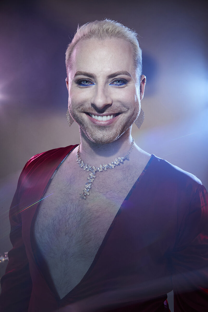 Vibrant studio portrait of Dain August with a smile, wearing a red outfit and dramatic lighting, photographed by Ylva Erevall.