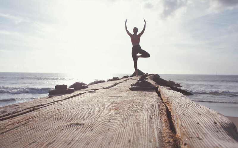 Man doing yoga in front of a beach, embracing wellness, breathwork, reiki, acupuncture and massage for healthy living.