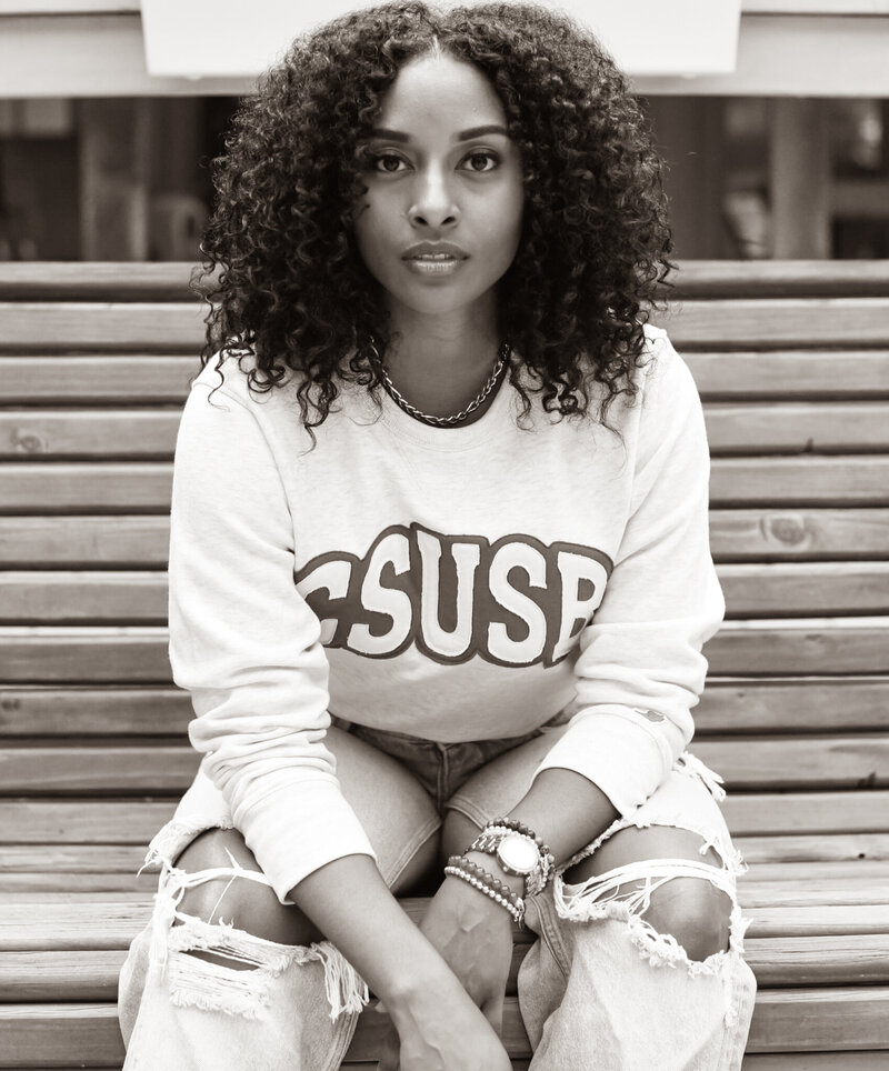 a high school senior sitting on a bench posing for a photo wearing a CSUSB sweater. photographed by Millz Photography in Greenville, SC