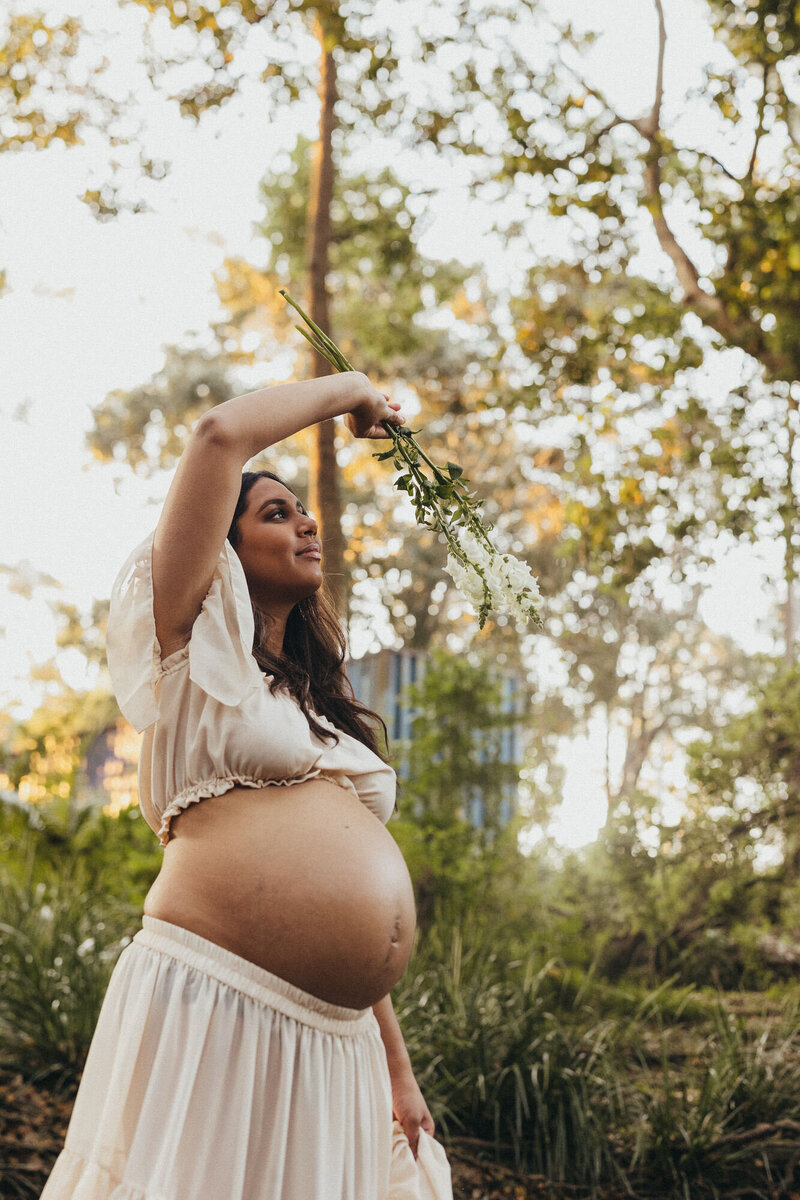 Maternity Photography of a pregnant mother at a creek location, waving flowers in front of her etherially